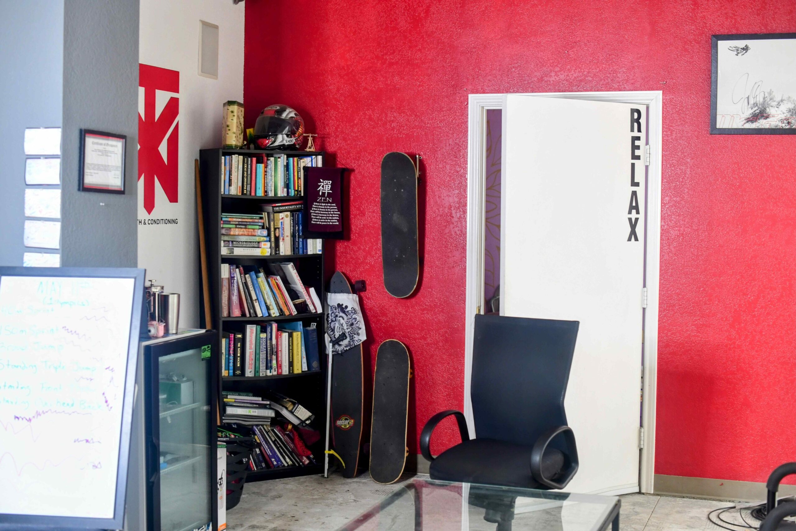 Cozy and inviting office space with a bookshelf filled with books, skateboards mounted on a red wall, a black office chair, and a door labeled 'RELAX', reflecting a relaxed and welcoming atmosphere.